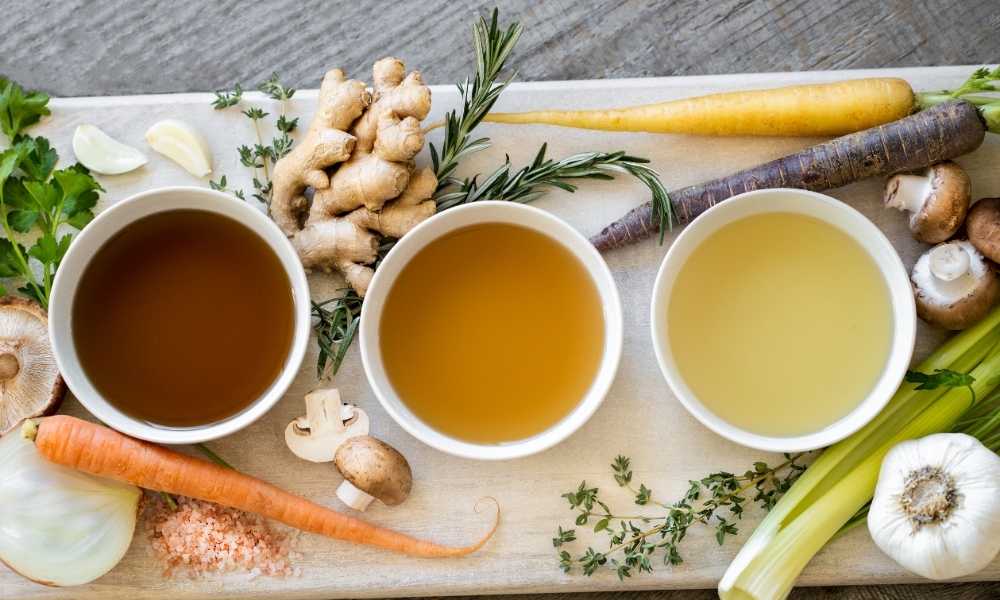 Fundos culinários dispostos em uma mesa com ossos e vários legumes e vegetais. Caldo claro, caldo de carne e caldo de ossos. bases essenciais para sopas e caldos.