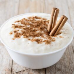 Arroz doce em uma tigela, decorado com canela em pó e pedaços de canela em pau.