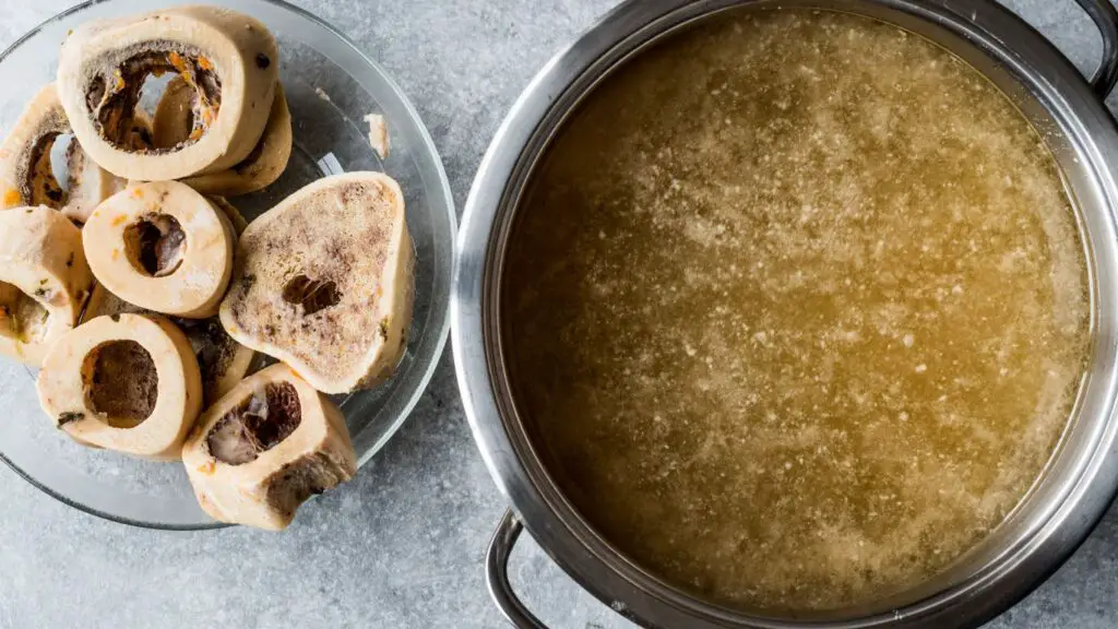 Panela contendo caldo de ossos recem cozido. Ao lado da panela estão os ossos utilizados para o preparo do caldo.