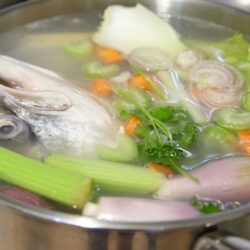 Panela com todos os ingredientes do caldo de peixa. Cabeça de peixe, legumes, aipo e outros.