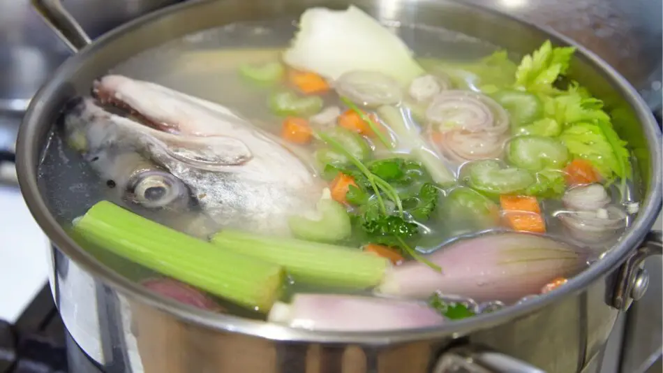 Panela com todos os ingredientes do caldo de peixa. Cabeça de peixe, legumes, aipo e outros.