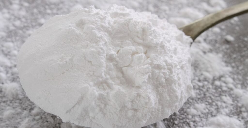 Pó branco e fino de açúcar de confeiteiro sendo peneirado sobre uma superfície escura.