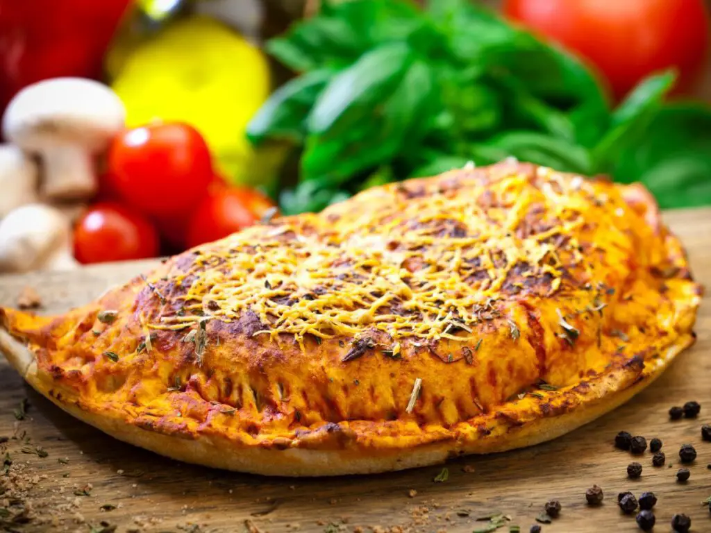 Calzone dourado e crocante, com bordas seladas e recheio de queijo derretido e molho de tomate visível.