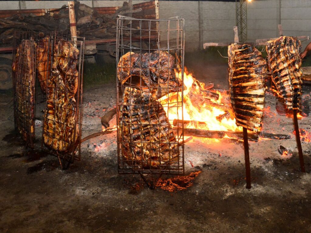 Churrasco gaúcho no chão, com espetos de carne fincados ao redor de uma fogueira em brasa.