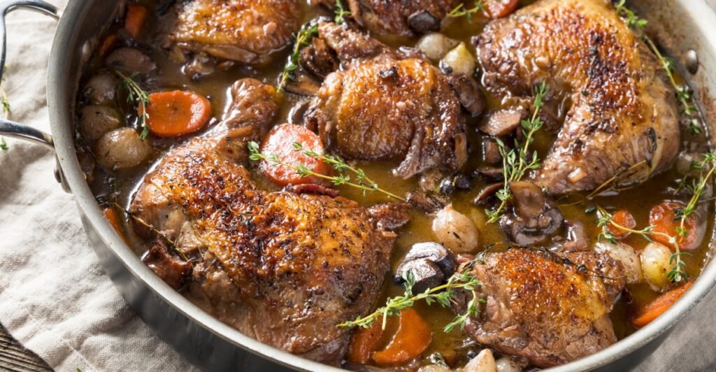 Coq au Vin servido com molho de vinho tinto, cogumelos e batatas, prato tradicional da culinária francesa.