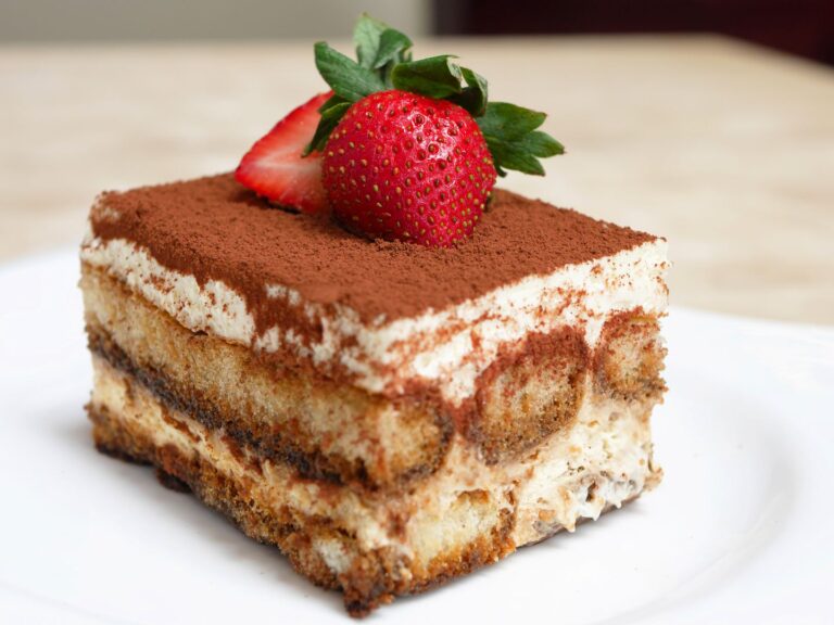 Tiramisù servido em uma travessa, com camadas de biscoito e creme de mascarpone, polvilhado com cacau e morangos.