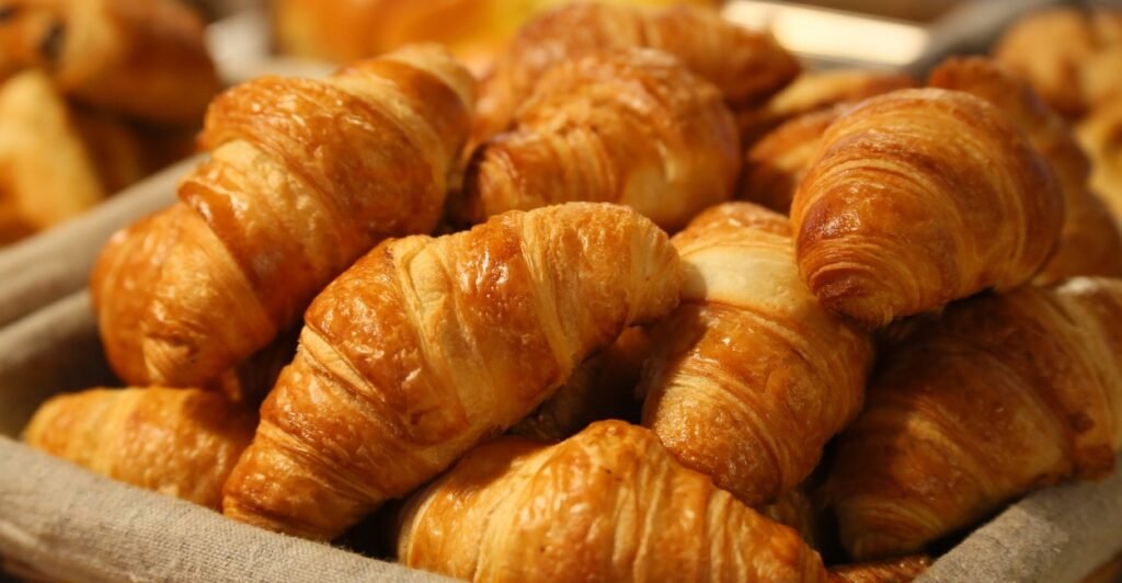 Croissant folhado e dourado, típico da culinária francesa, servido em prato de café da manhã.