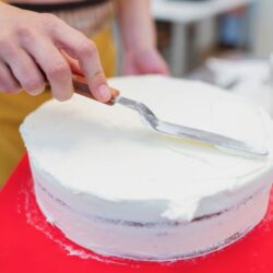 Bolo sendo coberto com glace branco utilizando uma espatula de confeiteiro.