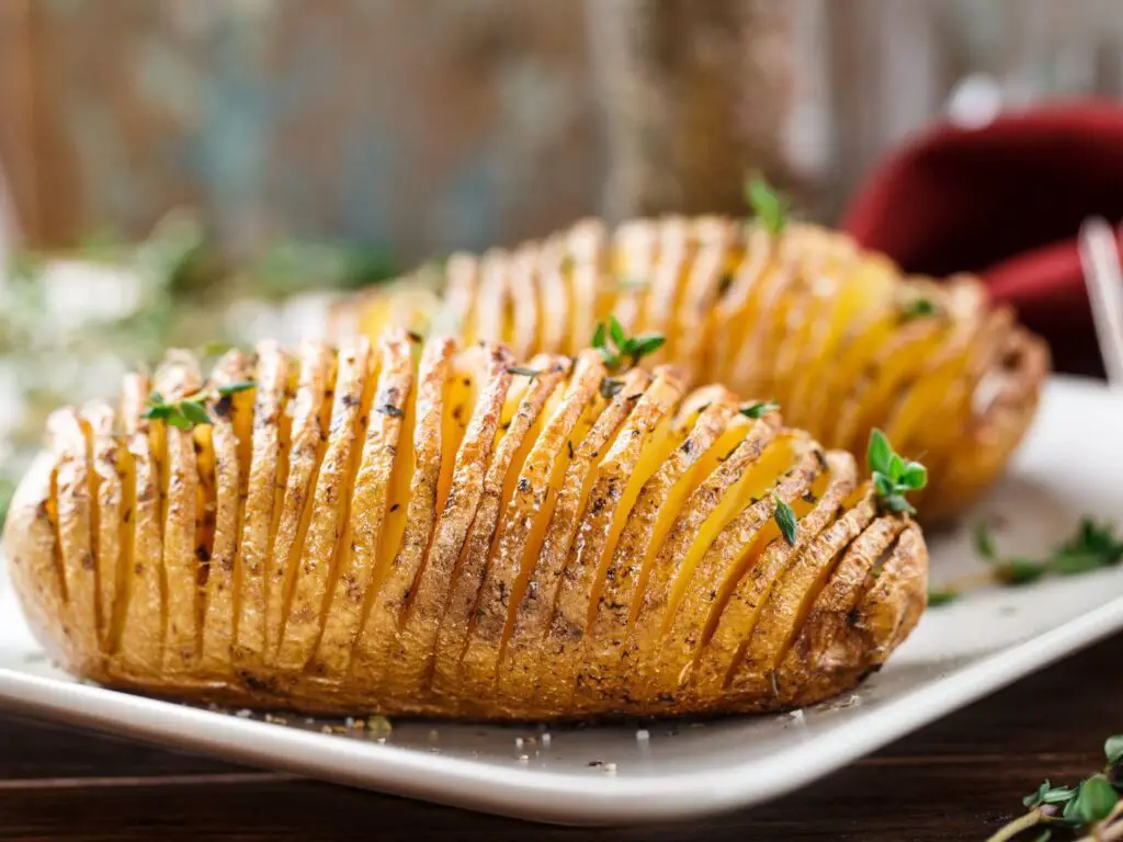 Batatas Hasselback douradas e crocantes, levemente temperadas e servidas em um prato rústico.