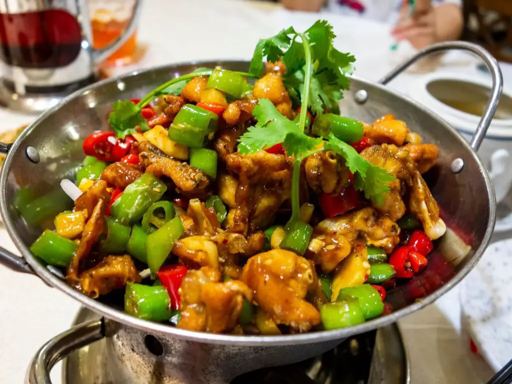 Hunan Chicken servido em um prato branco, com pedaços de frango salteados, legumes coloridos e molho picante.