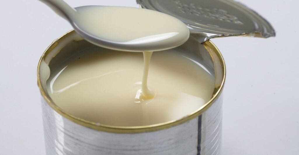 Lata aberta de leite condensado com colher cheia do creme doce e cremoso.