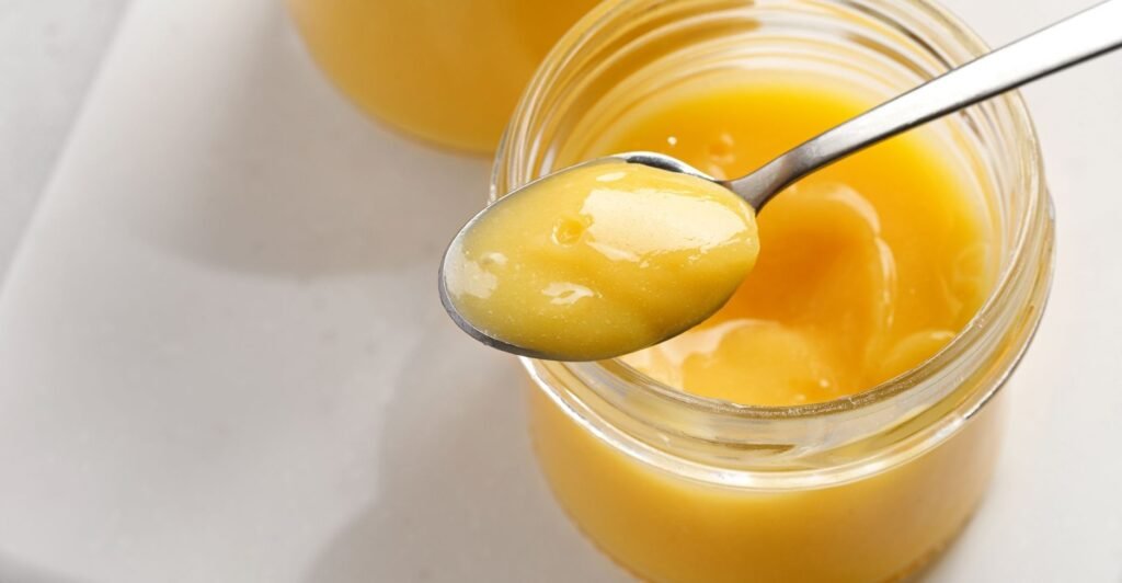 Pote de lemon curd amarelo vibrante com colher, creme de limão cremoso e brilhante.
