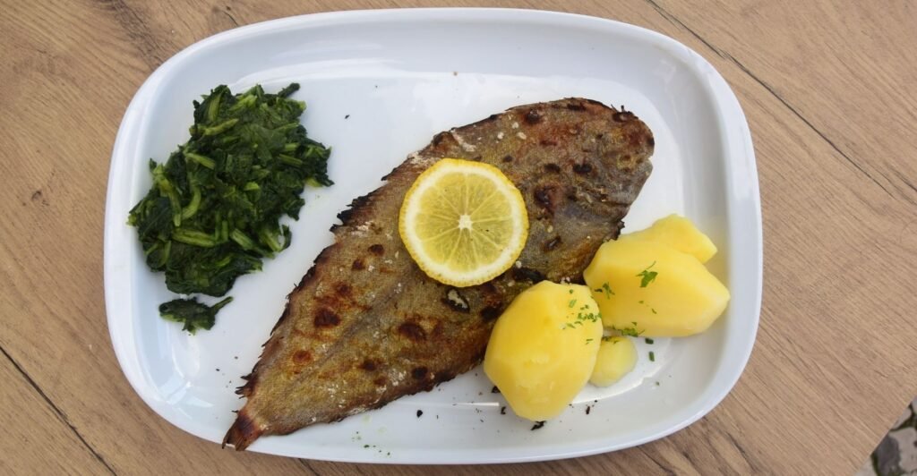 Filé de linguado grelhado com marcações douradas, servido com legumes e limão.