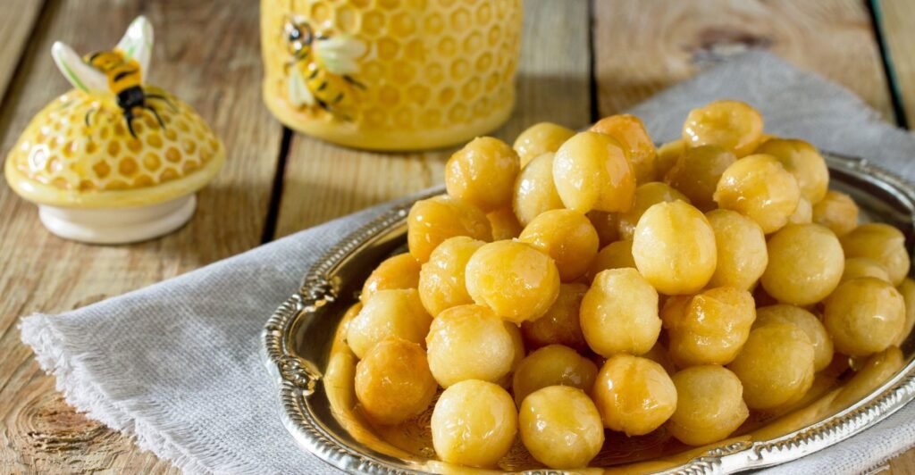 Porção de loukoumades dourados, cobertos com mel e polvilhados com canela.