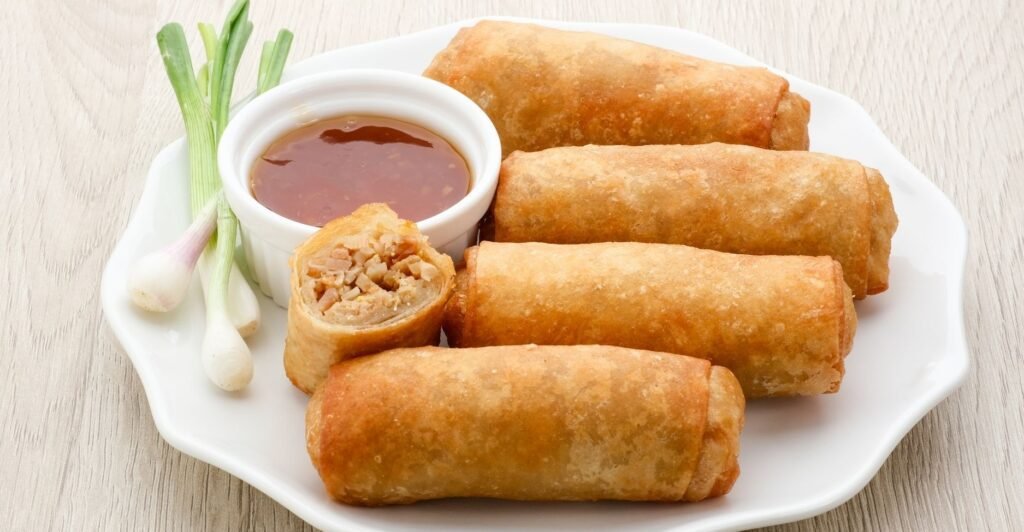 Rolinhos Lumpia fritos, crocantes e dourados, servidos com molho agridoce.