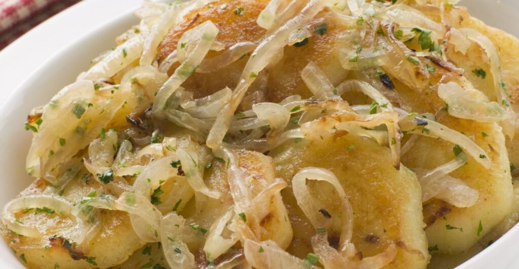 Batatas Lyonnaise douradas com cebolas caramelizadas, servidas em prato branco.