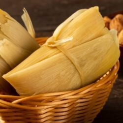 Pamonha doce embrulhada em palha de milho, servida em cesta de palha