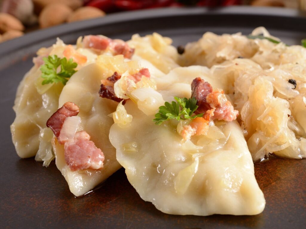 Pierogi cozidos servidos em um prato rústico, acompanhados de cebolas douradas e bacon.