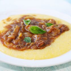 Polenta cremosa coberta com molho de carne, servida em um prato.