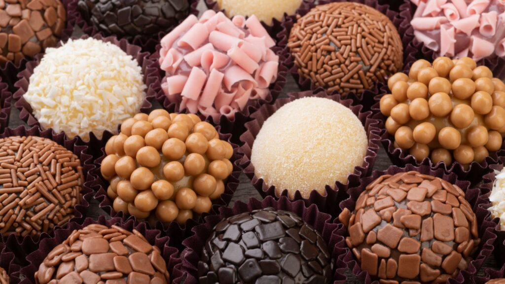 Brigadeiros gourmet em uma bandeja, com diferentes coberturas como chocolate granulado, coco ralado e chocolate picado e outros confeitos.