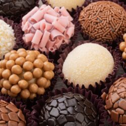 Brigadeiros gourmet em uma bandeja, com diferentes coberturas como chocolate granulado, coco ralado e chocolate picado e outros confeitos.