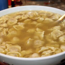 Sopa de capeletti servida em um prato fundo, com caldo claro e folhas de salsinha frescas.