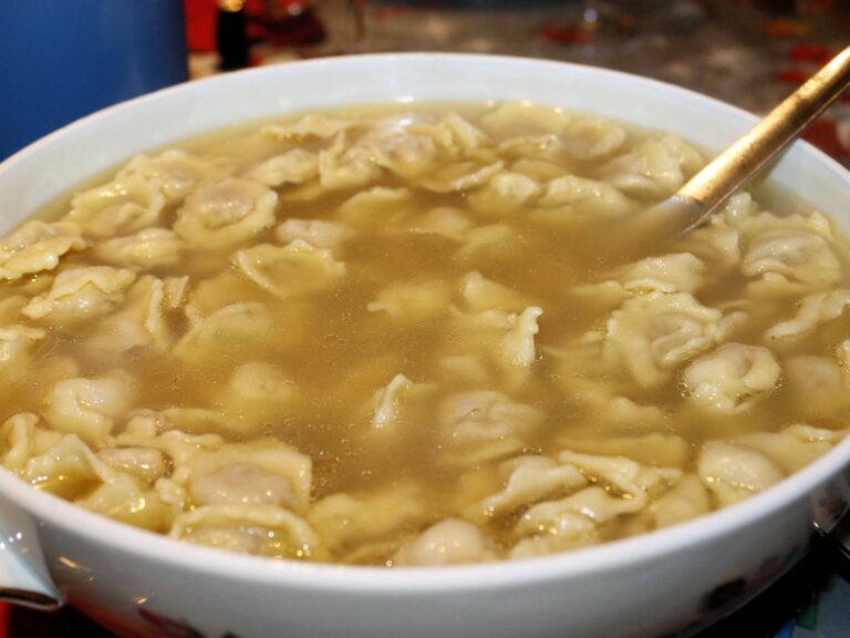 Sopa de capeletti servida em um prato fundo, com caldo claro e folhas de salsinha frescas.