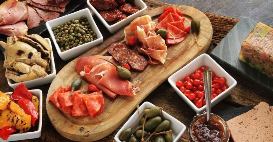 Tábua de antipasto com queijos, embutidos, azeitonas, tomates secos e pães artesanais sobre mesa rústica.