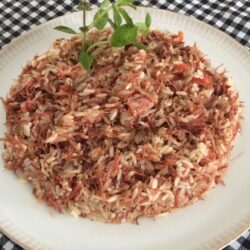 Arroz carreteiro servido em um prato branco, com carne seca desfiada e temperos frescos.