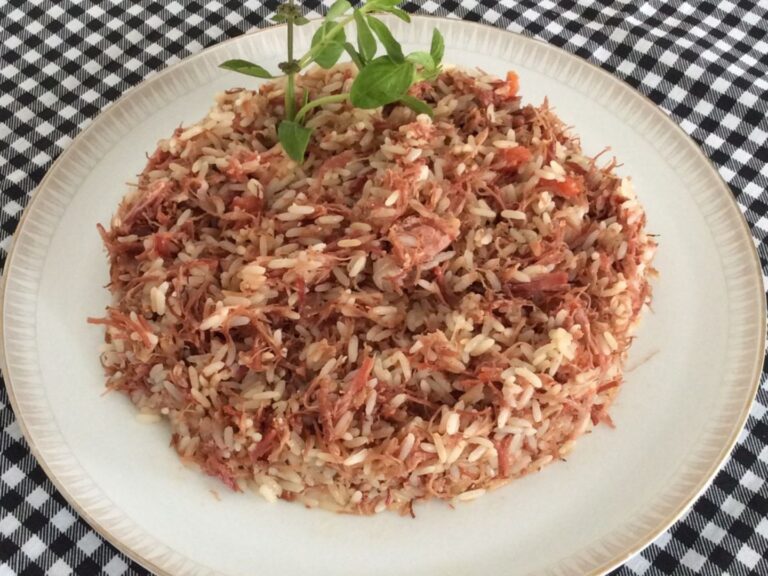 Arroz carreteiro servido em um prato branco, com carne seca desfiada e temperos frescos.