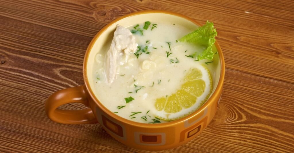Prato fundo com sopa avgolemono cremosa, decorada com salsinha picada, destacando sua textura suave e cor amarela pálida.