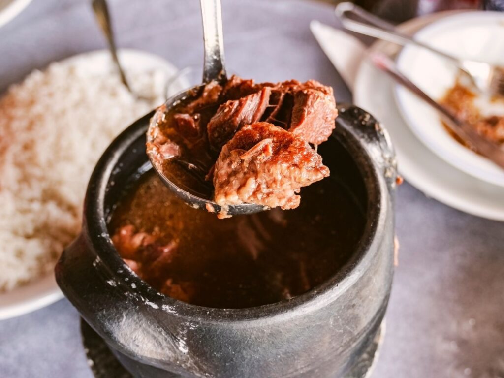 Barreado tradicional servido em uma panela de barro, acompanhado de farinha de mandioca e banana.