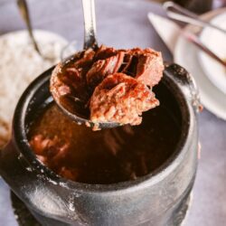 Barreado tradicional servido em uma panela de barro, acompanhado de farinha de mandioca e banana.