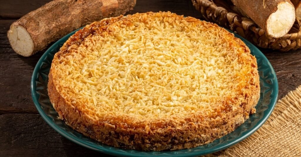 Bolo de mandioca cremoso cortado em pedaços, servido em prato rústico, comida de festa junina doce.