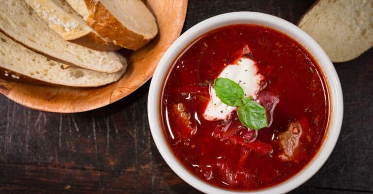 Tigela de borscht ucraniano com sour cream e endro fresco ao lado de pão de centeio.