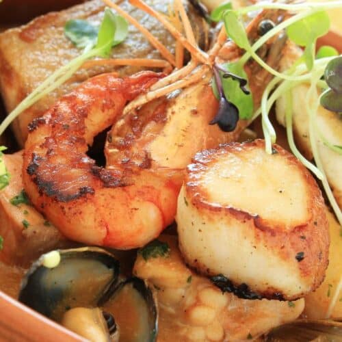 Tigela de bouillabaisse francesa com peixes, frutos do mar, ervas frescas e fatias de pão.