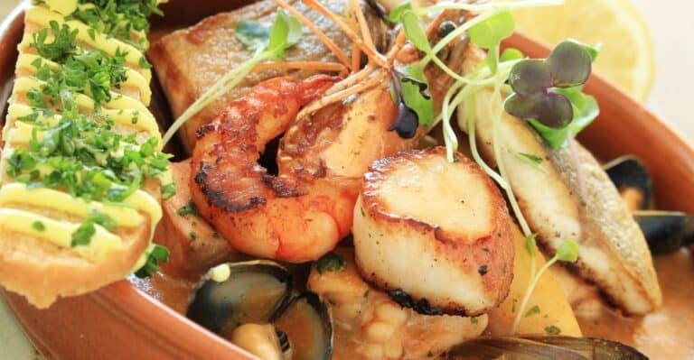Tigela de bouillabaisse francesa com peixes, frutos do mar, ervas frescas e fatias de pão.