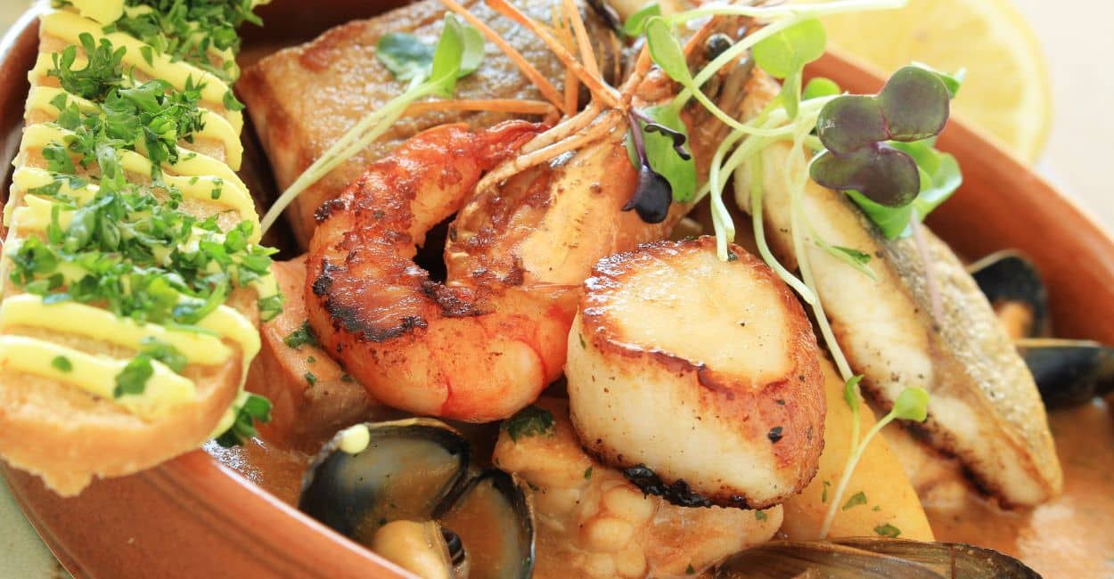 Tigela de bouillabaisse francesa com peixes, frutos do mar, ervas frescas e fatias de pão.