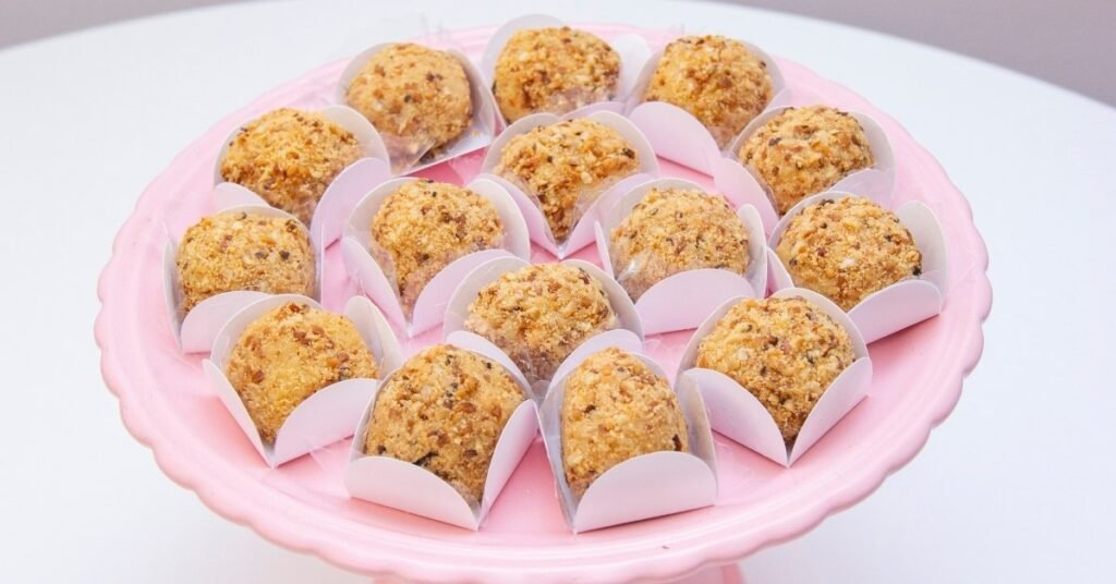 Brigadeiros de paçoca enrolados e cobertos com farofa de amendoim, servidos em forminhas, comida de festa junina doce.