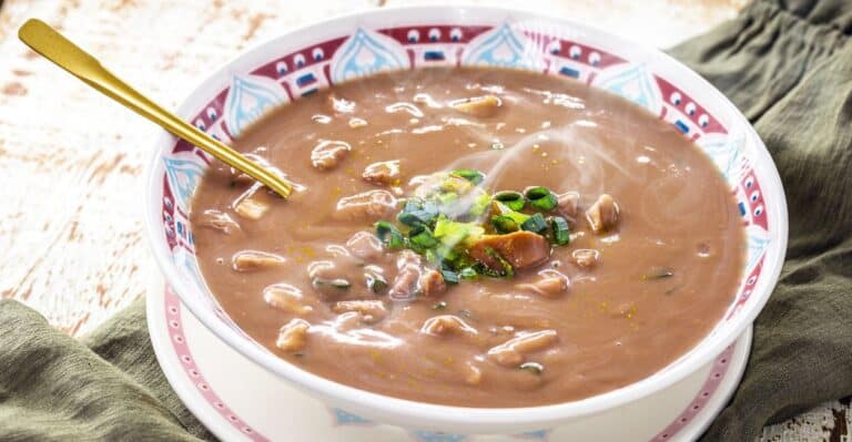 O caldo de feijão é uma receita clássica da culinária brasileira, apreciada em todas as regiões do país. Leve, nutritivo e cheio de sabor, esse prato combina feijão cozido, temperos aromáticos e, às vezes, carnes ou linguiça, resultando em uma refeição reconfortante, perfeita para dias frios ou para aquele momento em que se busca uma comida caseira e acolhedora. História do Caldo de Feijão O feijão é um dos alimentos mais tradicionais do Brasil desde a colonização, sendo base da alimentação diária das famílias. O caldo de feijão surgiu como uma maneira de aproveitar o feijão cozido, transformando-o em uma sopa nutritiva e saborosa. Ao longo do tempo, diferentes regiões do país adaptaram o caldo: No Sudeste, é comum adicionar linguiça ou bacon. No Nordeste, pode incluir temperos como coentro e pimenta-de-cheiro. No Sul, às vezes recebe carnes defumadas ou paio. Esse prato é símbolo da cozinha afetiva brasileira, trazendo lembranças de refeições familiares e momentos de conforto à mesa. Características e Sabores do Caldo de Feijão Sabor intenso e reconfortante, que destaca o feijão e os temperos. Textura cremosa, quando batido parcialmente ou cozido até desmanchar. Versatilidade: pode ser servido puro, com carnes ou até com legumes. Aroma acolhedor, graças à combinação de alho, cebola, folhas de louro e temperos regionais. Dicas para um Caldo de Feijão Perfeito Use feijão de boa qualidade, preferencialmente deixado de molho por algumas horas. Cozinhe com temperos aromáticos, como alho, cebola e louro, para intensificar o sabor. Bata parcialmente o feijão cozido para obter uma textura cremosa, se desejar. Finalize com carnes defumadas ou linguiça para uma versão mais robusta. Sirva quente, acompanhado de arroz branco, torresmo ou pão caseiro. Curiosidades sobre o Caldo de Feijão É considerado um prato de conforto e muito presente em mesas familiares no Brasil. Em algumas regiões, o caldo de feijão é servido como entrada ou prato principal, dependendo da consistência. O caldo de feijão é uma forma econômica e nutritiva de aproveitar ingredientes do dia a dia, mantendo a tradição da cozinha brasileira. Harmonizações O caldo de feijão combina muito bem com: Arroz branco ou integral Carnes assadas ou defumadas Pão caseiro ou torradas Ervas frescas, como cebolinha ou salsinha, para realçar o sabor Conclusão O caldo de feijão é mais que uma sopa: é uma expressão da culinária brasileira, que combina tradição, sabor e conforto em uma única receita. Nutritivo, versátil e fácil de preparar, ele continua sendo um prato indispensável nas refeições familiares em todo o país.