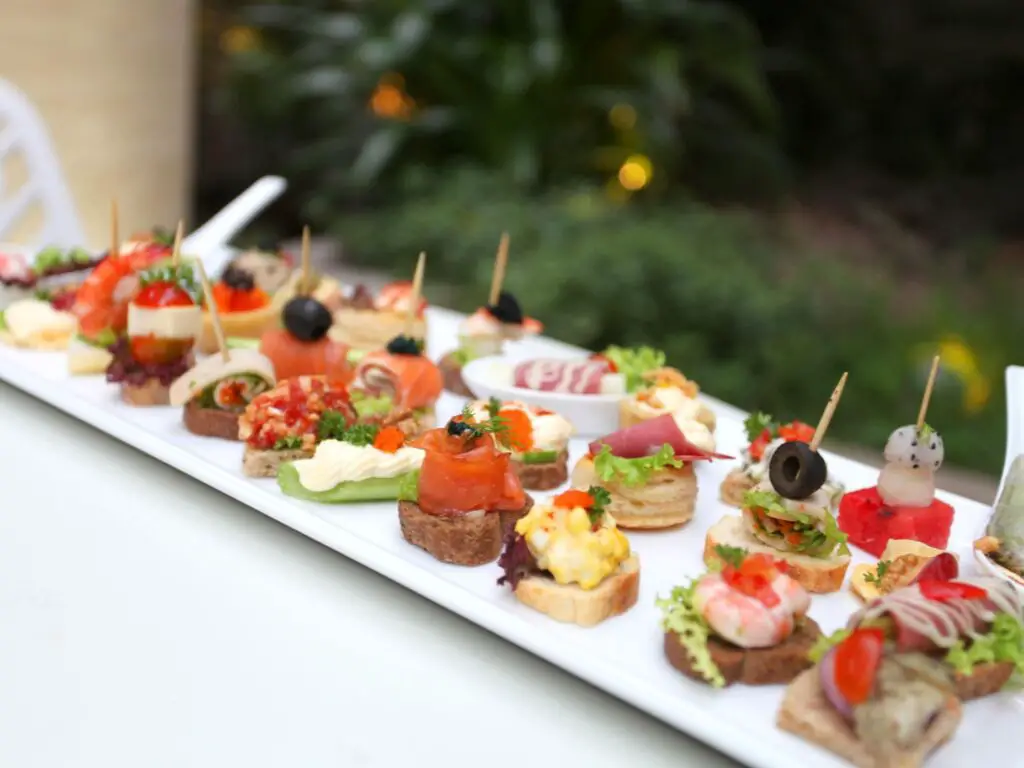 Canapés variados com diferentes coberturas coloridas, dispostos em uma bandeja elegante.