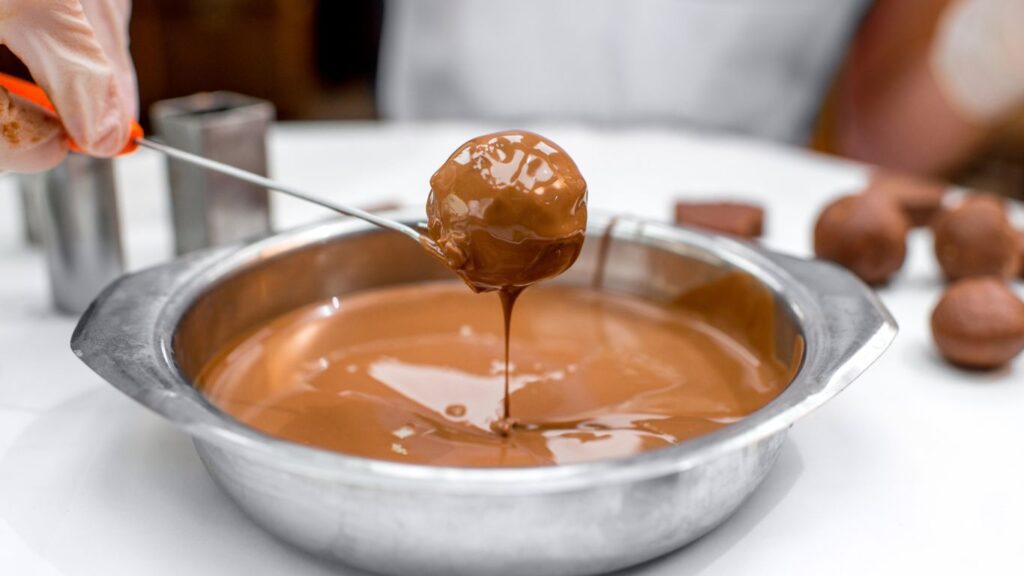 Bombom sendo coberto com chocolate derretido, criando uma camada lisa e brilhante.