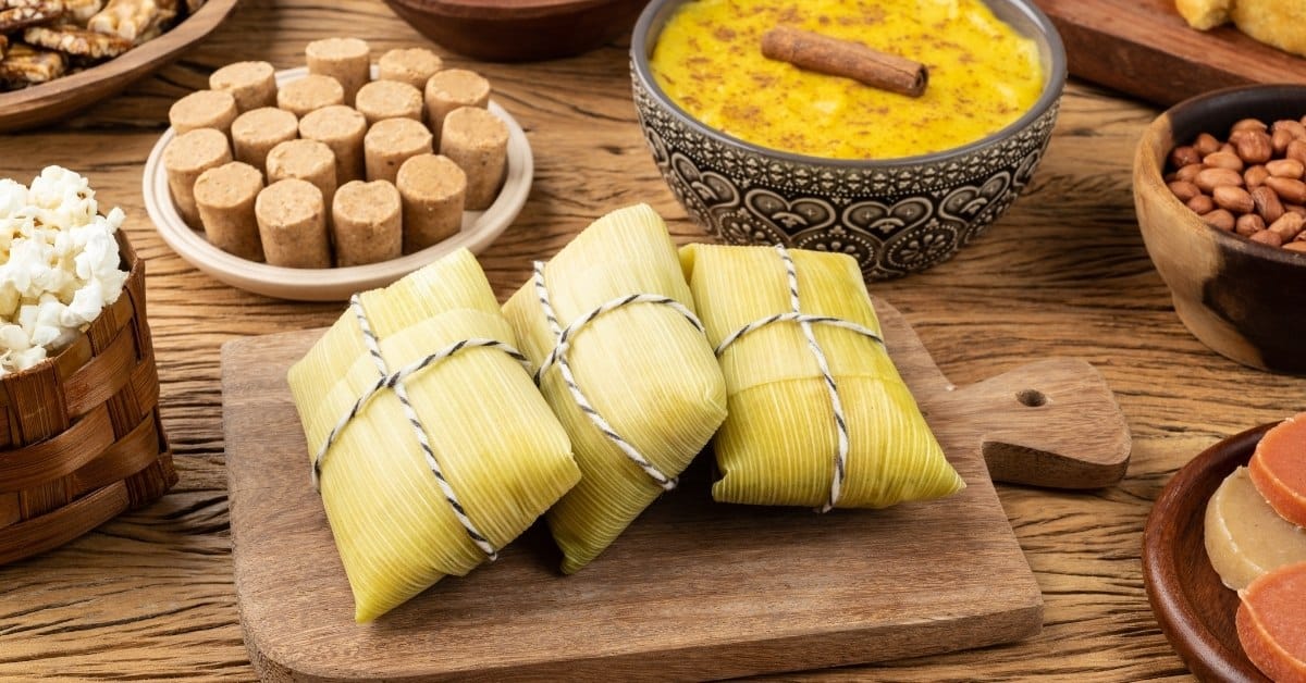 mesa com comida de festa junina doce. opçoes como pamonha, paçoca, curau e muitos outros.