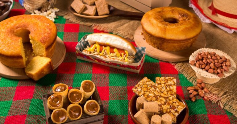 Mesa decorada com diversas comidas típicas de festa junina como canjica, pamonha, bolo de fubá, milho cozido e pé de moleque