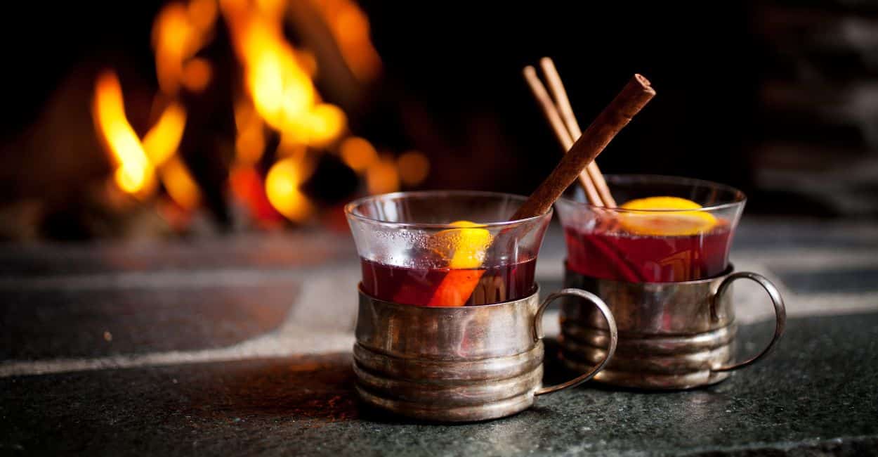 copos com vinho quente e uma fogueira ao fundo. descubra como fazer vinho quente em casa.