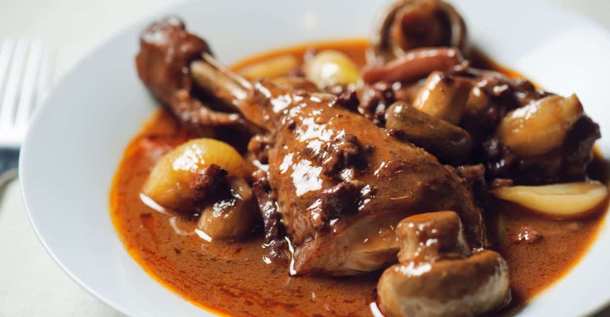 Tigela de coq au vin francês com frango, cogumelos, cebolas caramelizadas e molho de vinho tinto.
