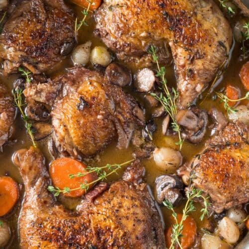 Panela finalizando a receita de coq au vin francês com caldo de vinho, legumes e temperos tradicionais.