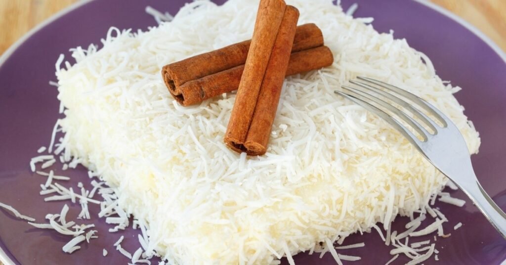 Cuscuz de tapioca com coco, cortado em pedaços, servido em prato rústico, comida de festa junina doce.