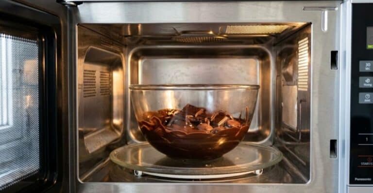Chocolate meio amargo picado em uma vasilha de vidro sendo derretido dentro de um micro-ondas.
