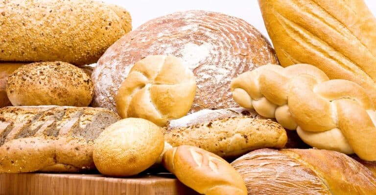 Mesa rústica com diversos tipos de pães artesanais — pães de fermentação natural, baguetes, brioches, pães integrais e pães de forma — dispostos de forma apetitosa, simbolizando o Dia Mundial do Pão.